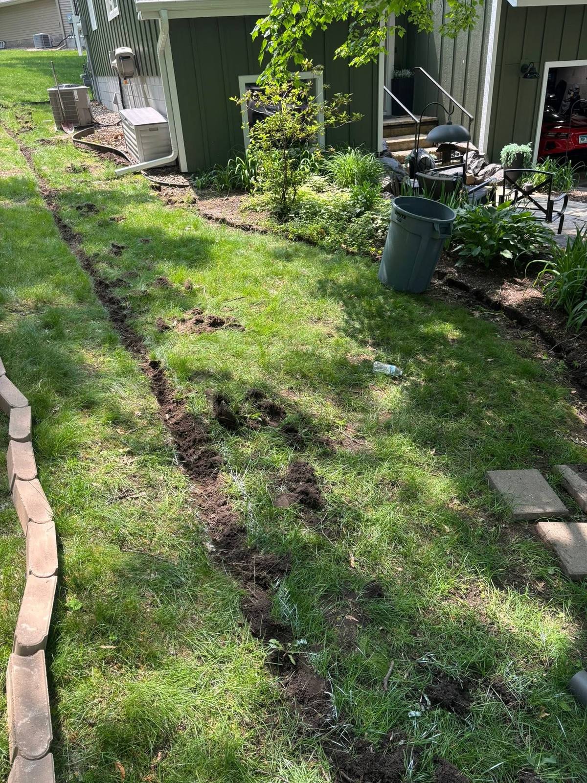 A bed line along the side of a house cleared back to bare soil, with debris removed and the edge cut clean.