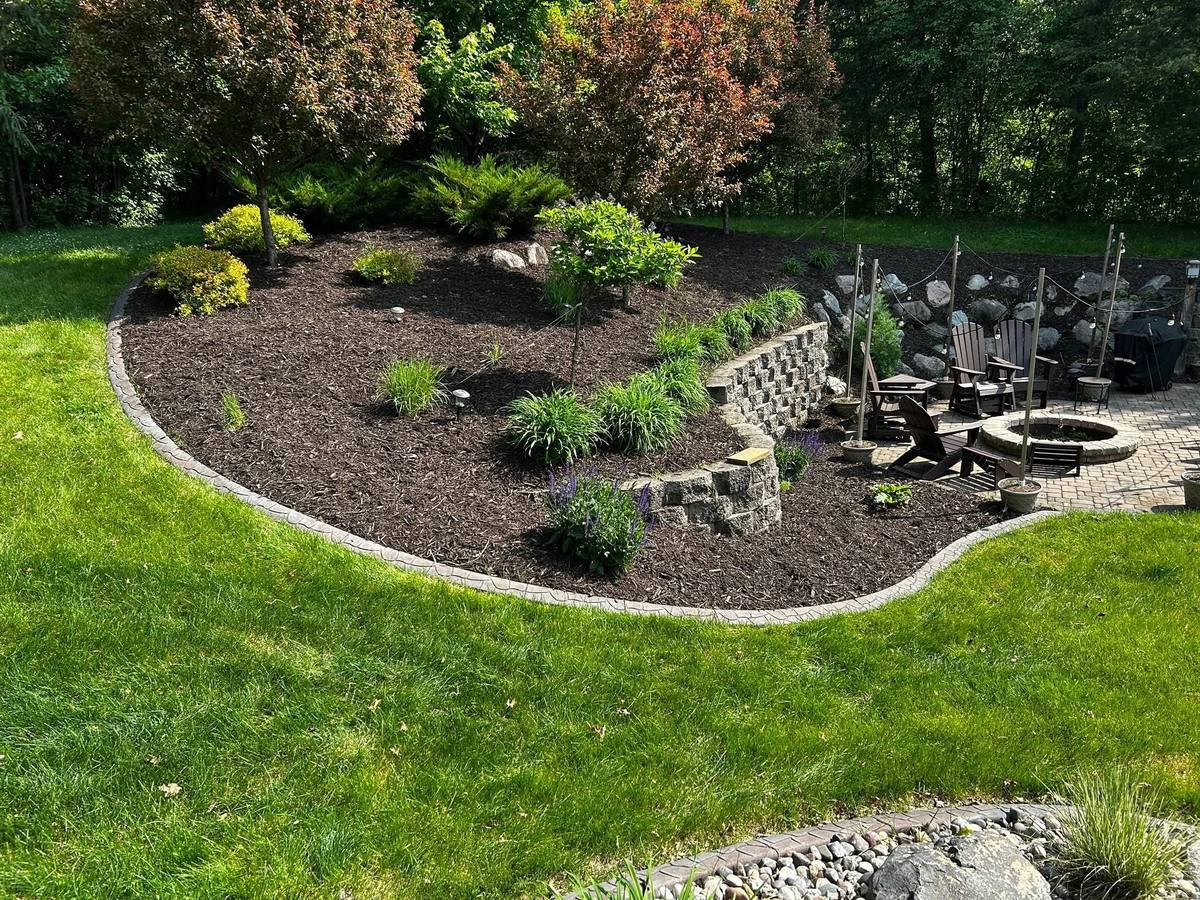 A curved landscape bed finished with fresh dark mulch around established plantings and a seating area.